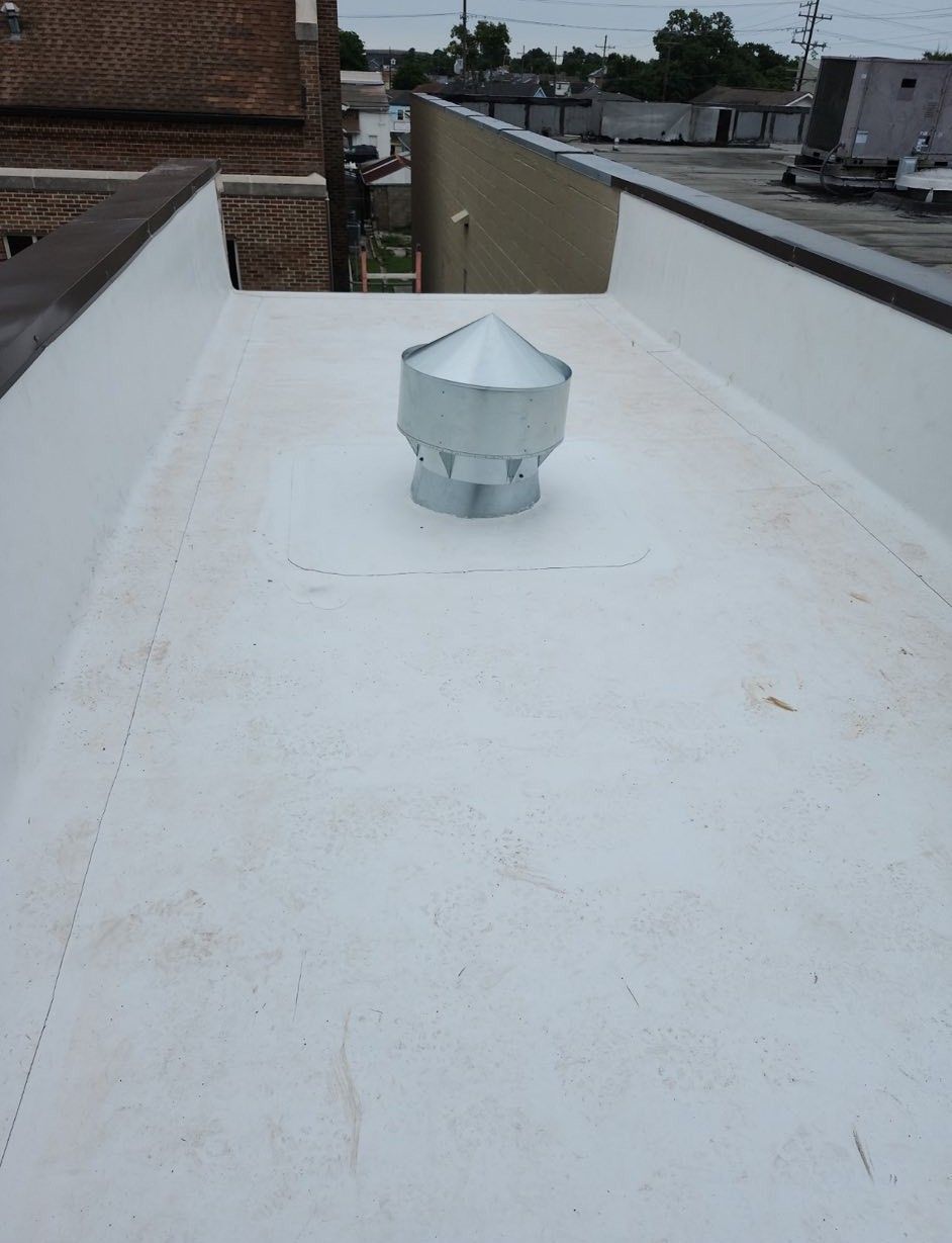 Flat white roof with a metal vent cap. Brick building in the background.