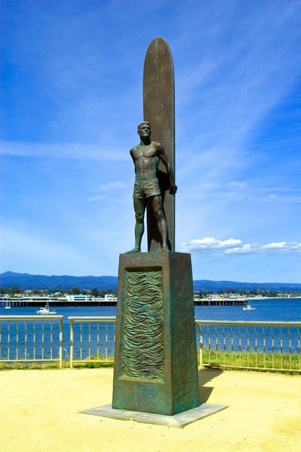 A statue of a man holding a surfboard in front of a body of water.