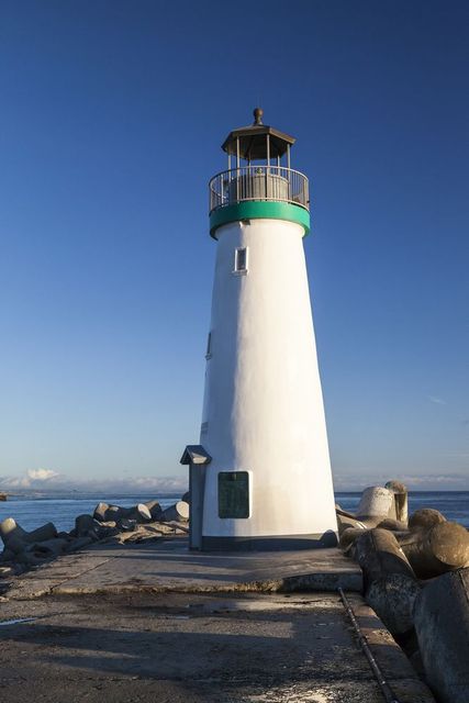 A white lighthouse with a green top is sitting on a pier overlooking the ocean.