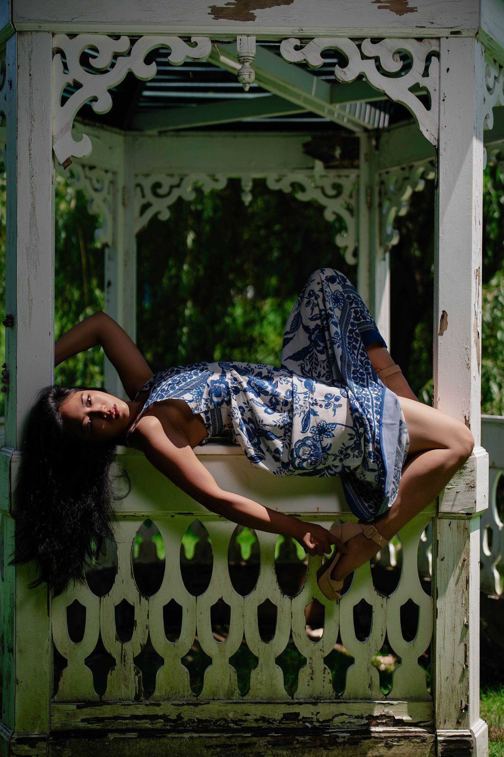 NYC model Minnie Lee —by Alexis Pesante reclines in a white gazebo, wearing blue and white patterned clothing, gazing at the camera.