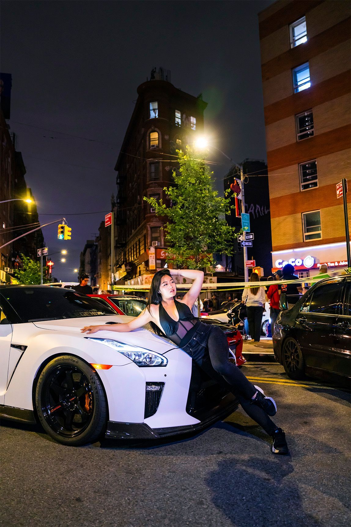 Woman posing on a white sports car at night in a city.