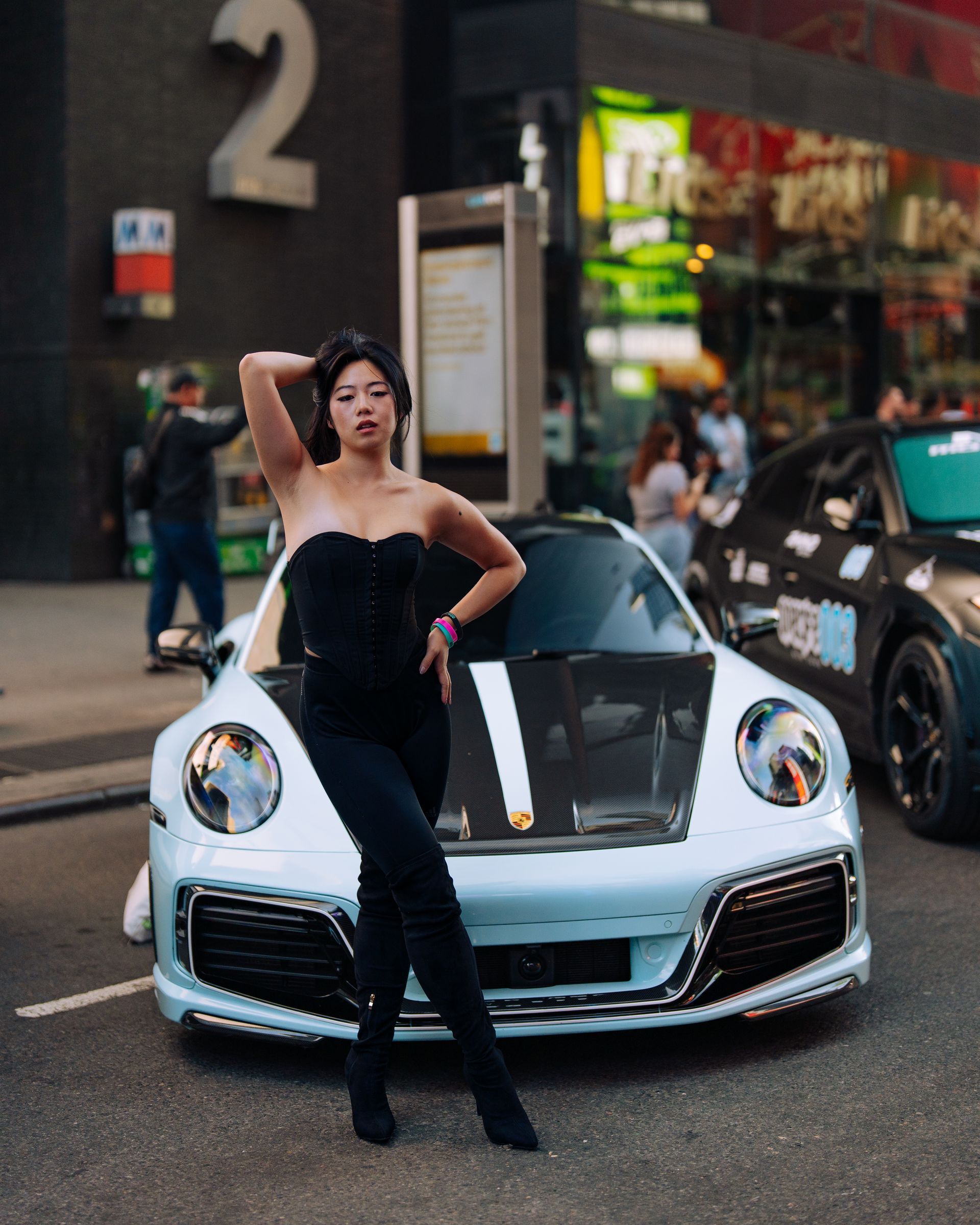 Minnie Lee - NYC model in black outfit poses in front of a Porsche car,  at Times Square, NYC One Life Car Rally.
