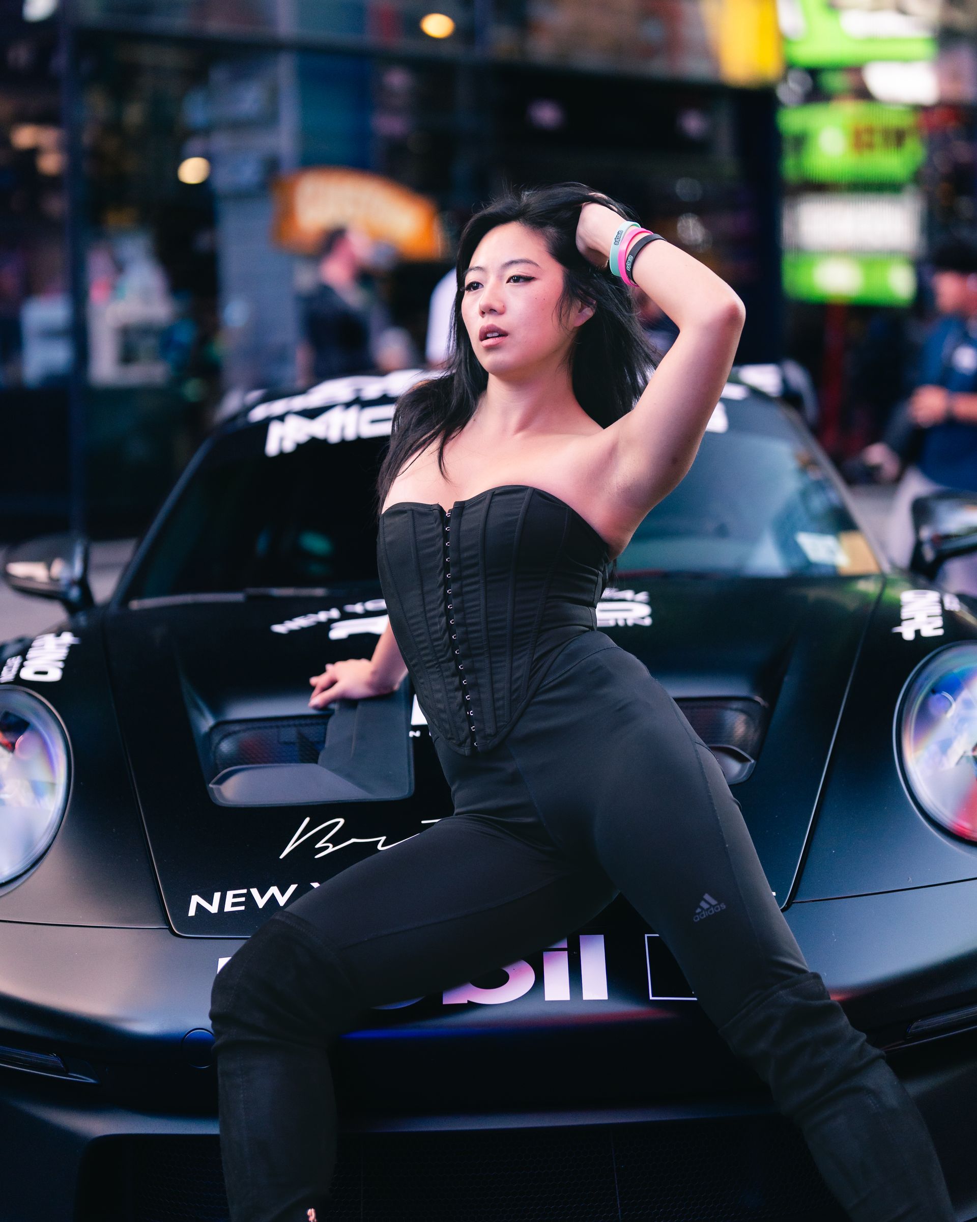 Minnie Lee - NYC model in black outfit poses in front of a black Porsche car,  at Times Square, NYC One Life Car Rally.