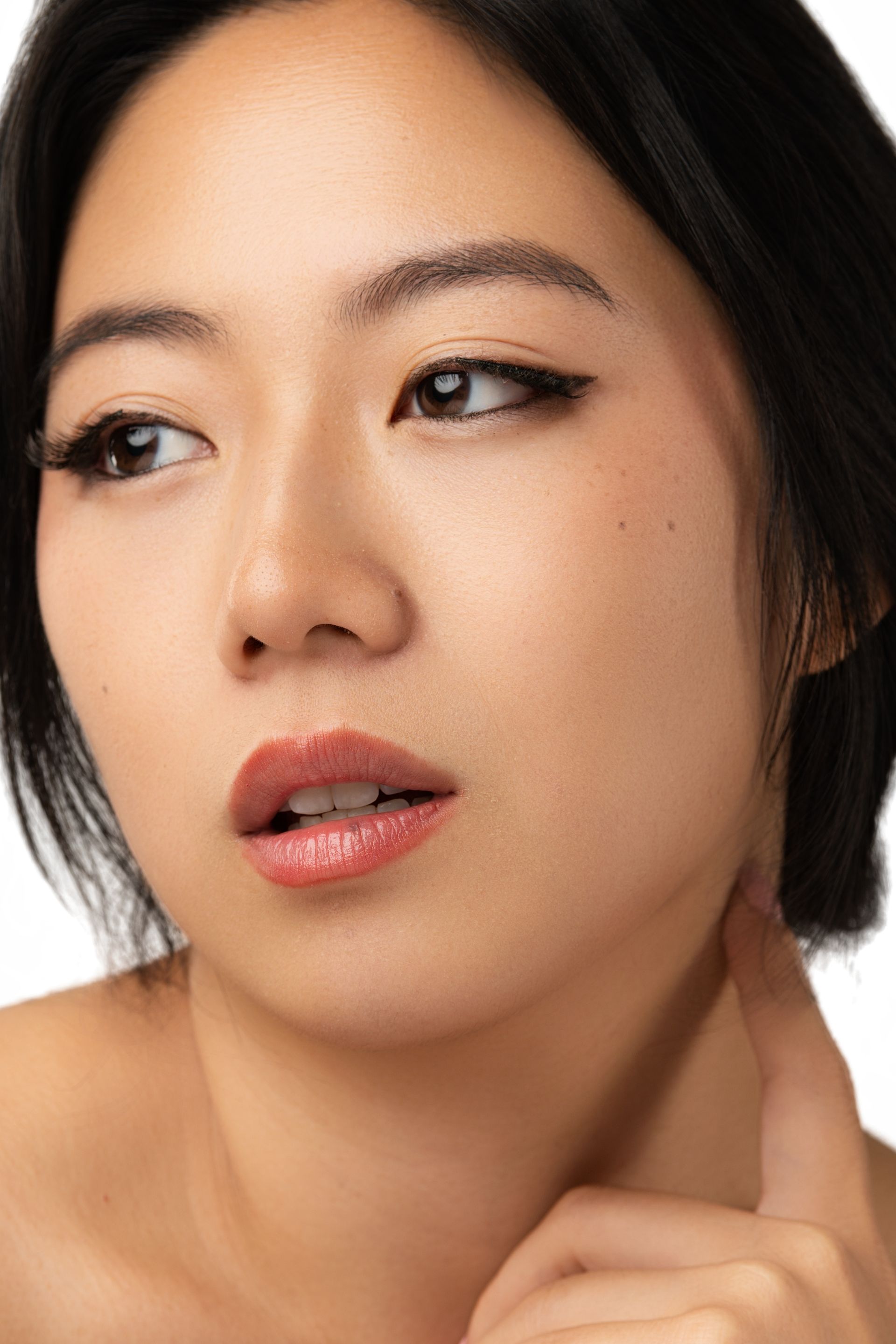 Woman with dark hair, brown eyes, and a slight smile, touching her neck. K beauty