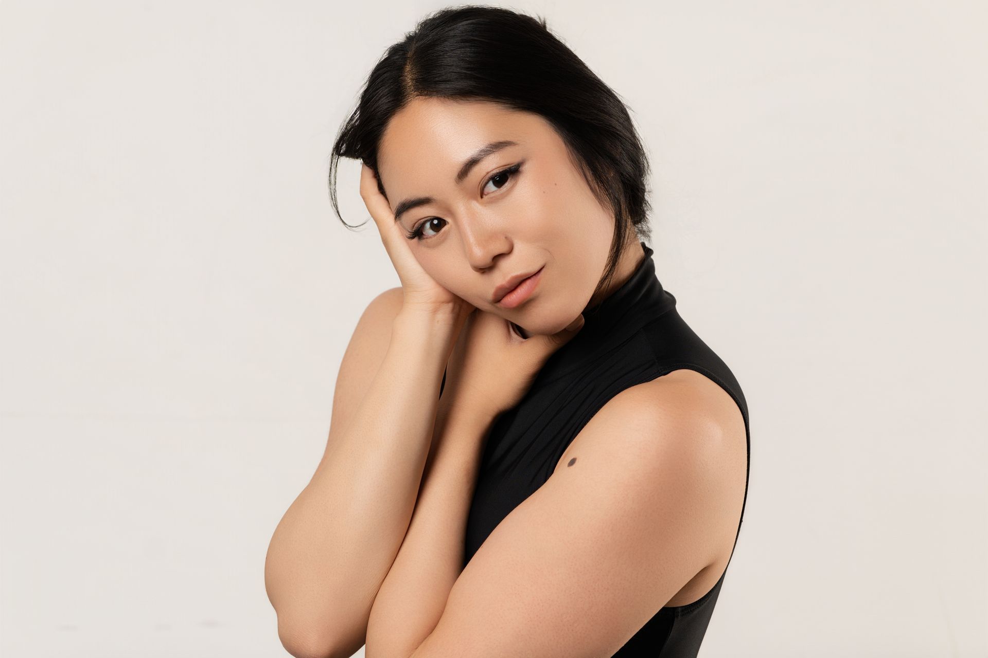 Woman with black hair and top, poses with hand on her face, smiles at the camera.