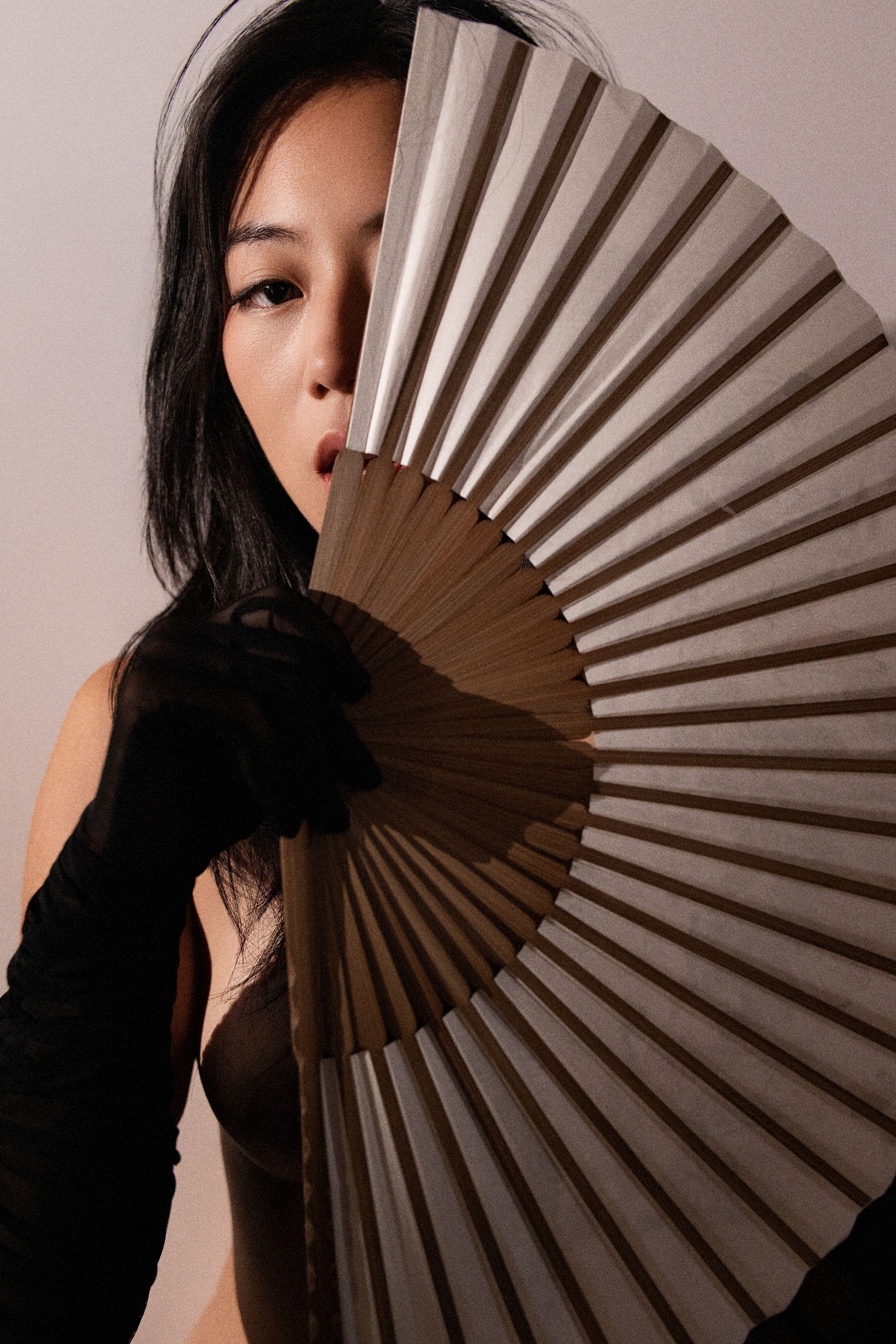 NYC model Minnie Lee in an elegant fine-art nude photo set, posed with a flowing hand-fan and long black gloves, her form sculpted by soft light; captured by Orion Mckinley Phillips II in a sophisticated, timeless editorial style.