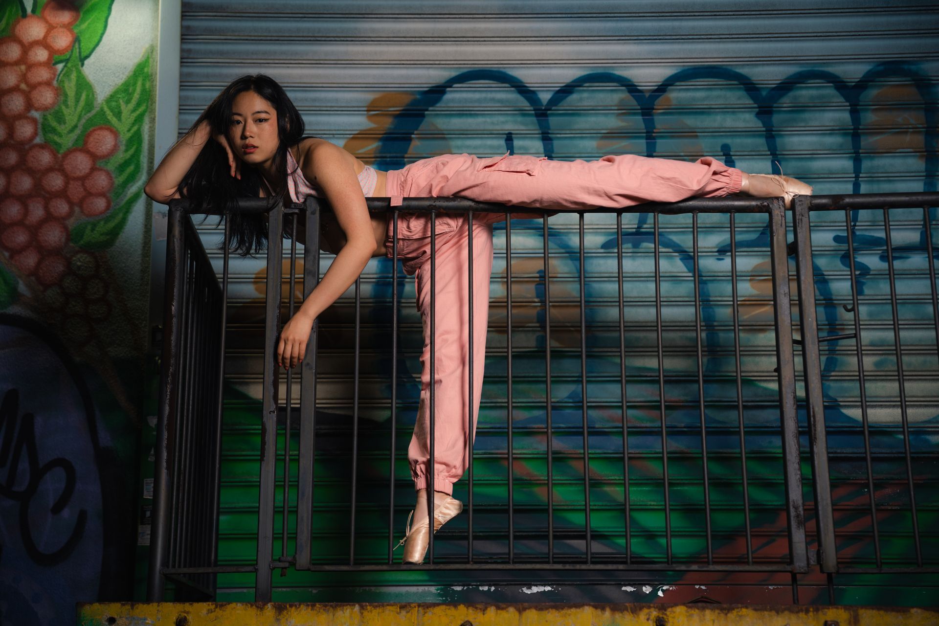 Ballet model in pink pants and pointe shoes rests on a graffiti-covered railing.