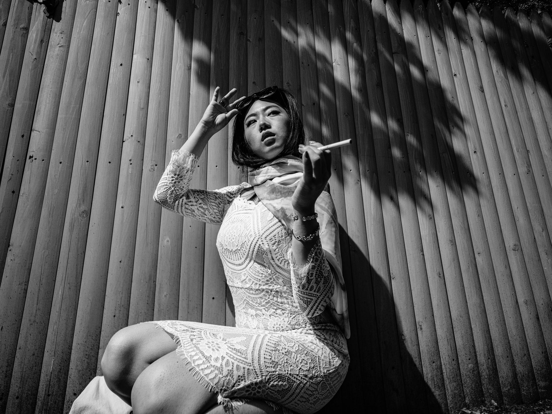 Woman in white dress playing a flute, leaning against a corrugated wall, shadows.