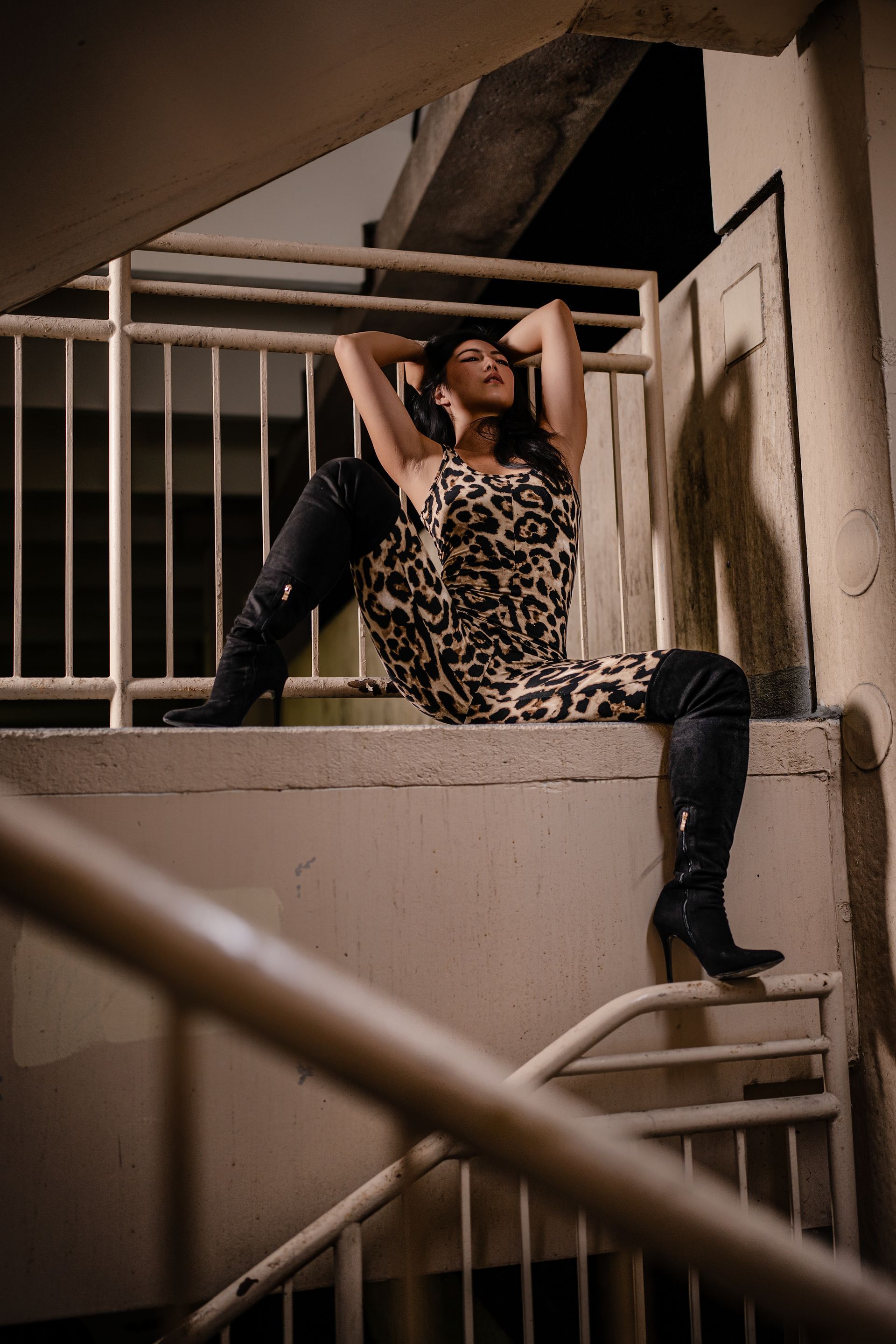 NYC model Minnie Lee in leopard print dress and black boots poses on outdoor steps, hands behind head.