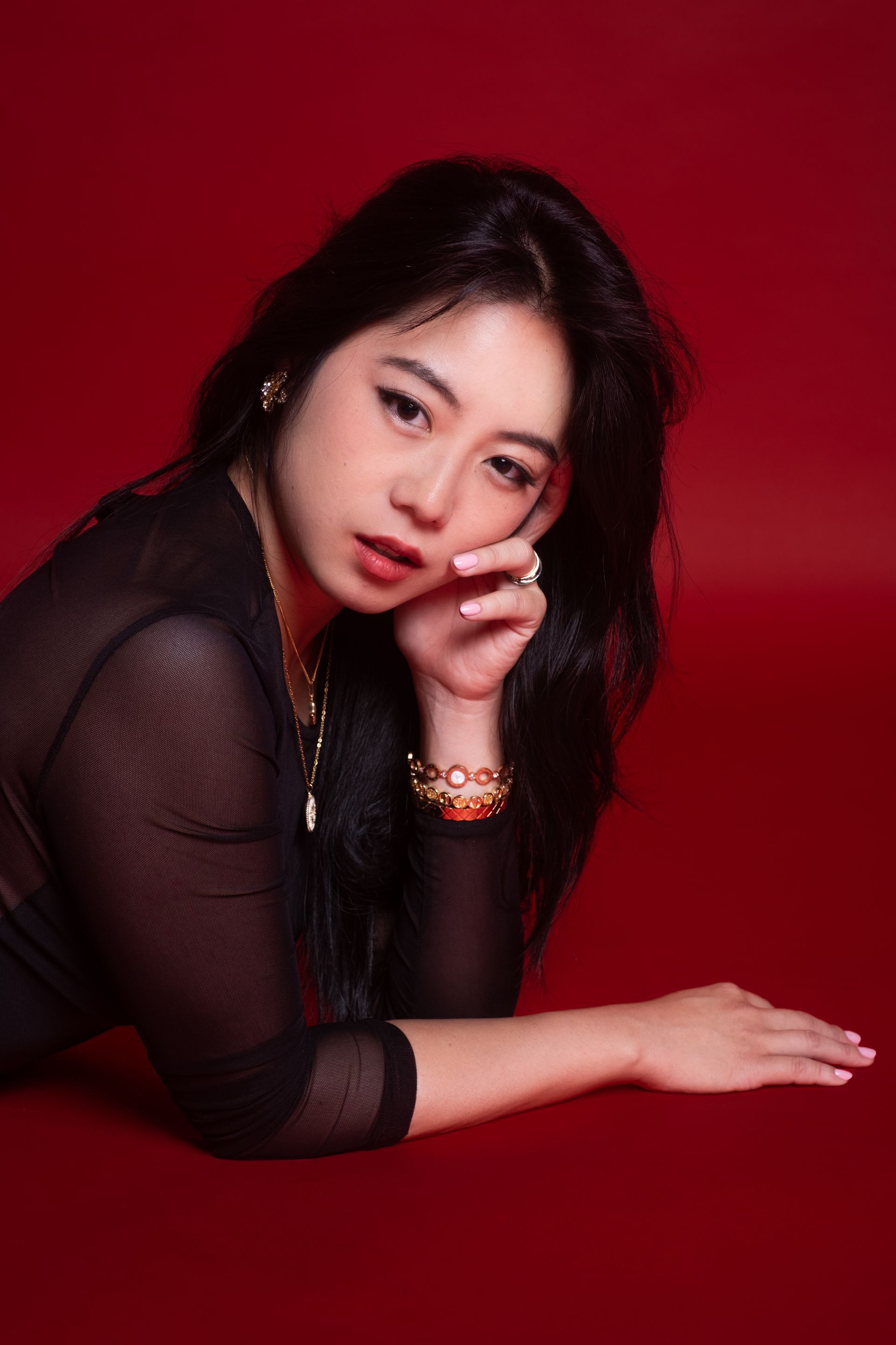 Luxury editorial portrait in controlled red studio light, disciplined posture and sculptural lines, model Minnie Lee.
