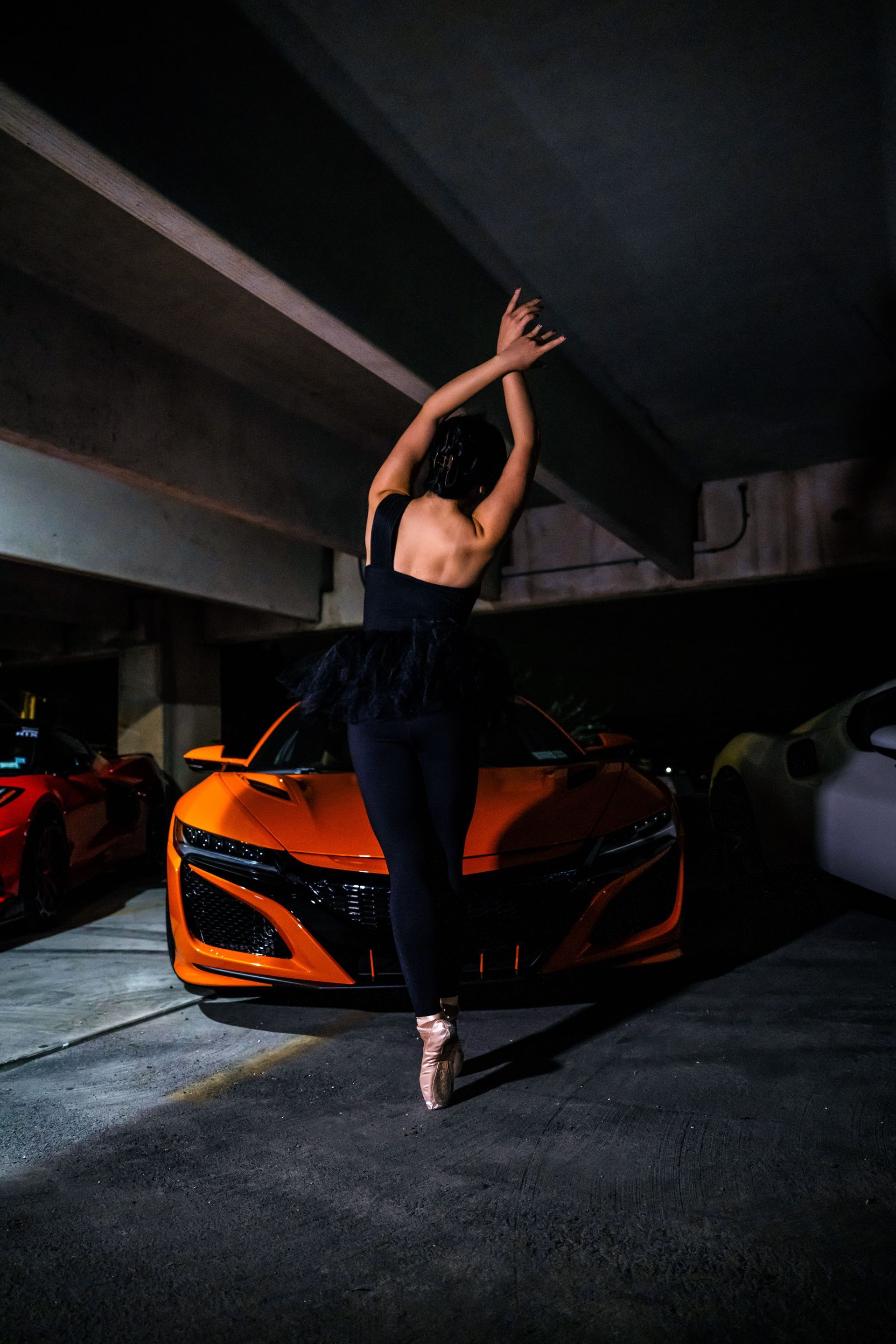 Model Minnie Lee performing ballet en pointe in front of an orange Acura NSX during the Cars x Ballet shoot at the Checkm8 car meet, photographed by Josanna Uy