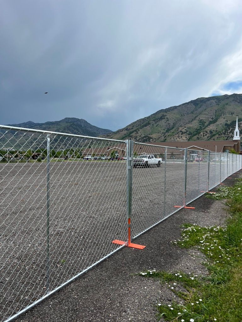 Chain-link fence beside gravel lot with mountains and cloudy sky in the background