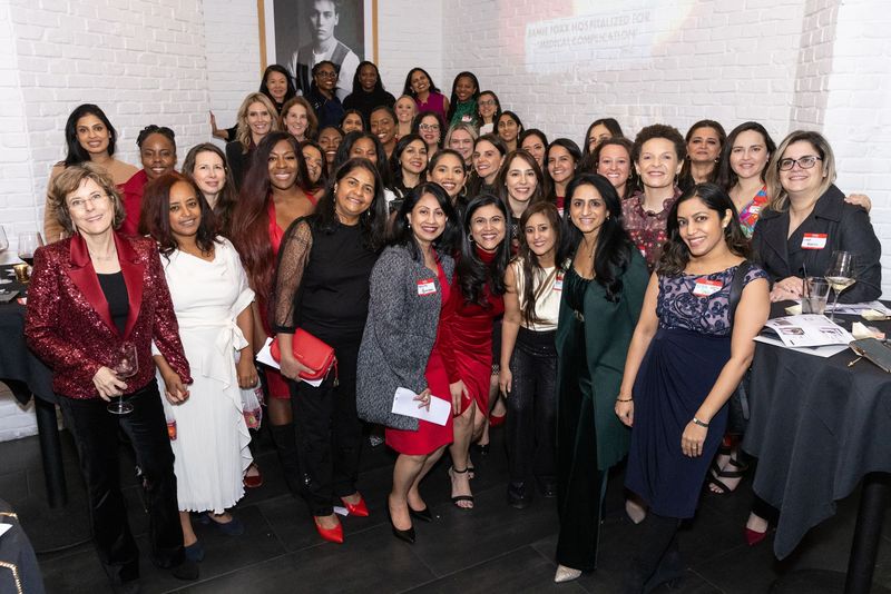 Group of people posing indoors at a formal event, many in red and black outfits, smiling in front of a banner