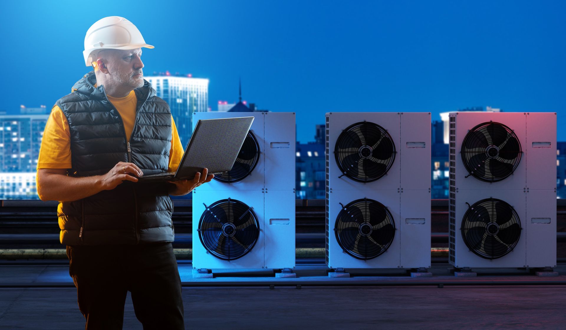 HVAC technician with laptop inspecting rooftop air conditioning units at night.