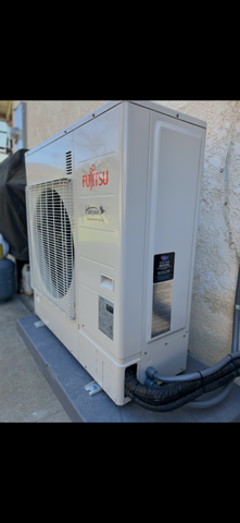 Man cleaning an AC unit with spray bottle and sponge. White wall backdrop.
