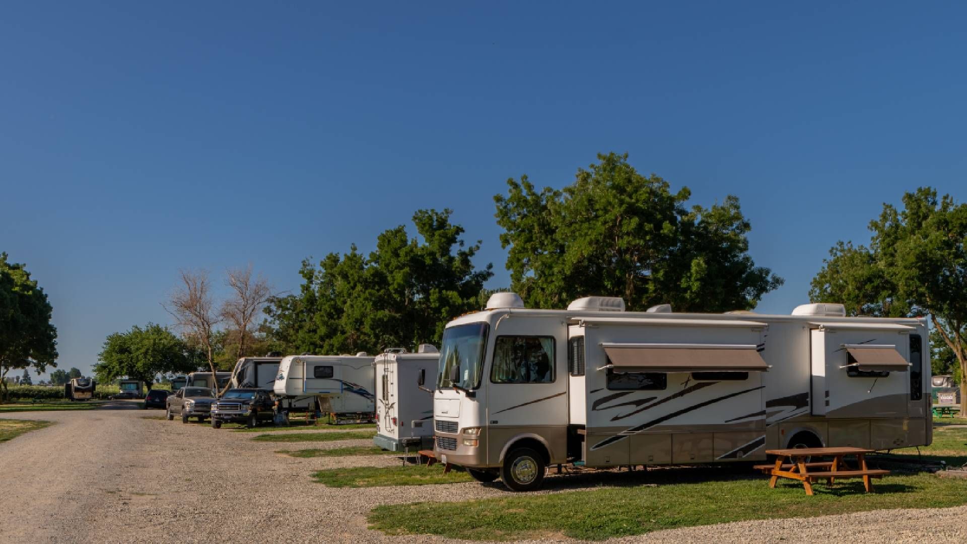 RV campground with several recreational vehicles parked on gravel sites under a blue sky.