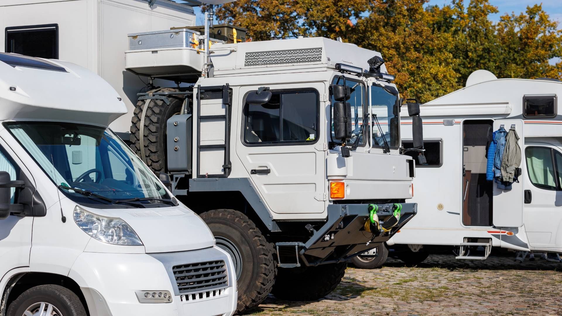 White RVs and an off-road truck parked outdoors on a sunny day.