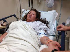 A woman is laying in a hospital bed with a man holding her hand.