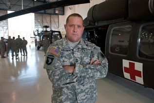 A man in a military uniform is standing in front of a helicopter with his arms crossed.