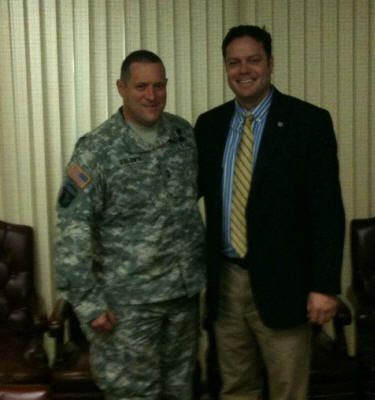 A man in a suit stands next to a man in a military uniform
