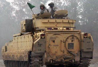 Two soldiers are riding on top of a military tank.