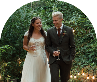 A bride and groom are walking down a path holding champagne glasses.