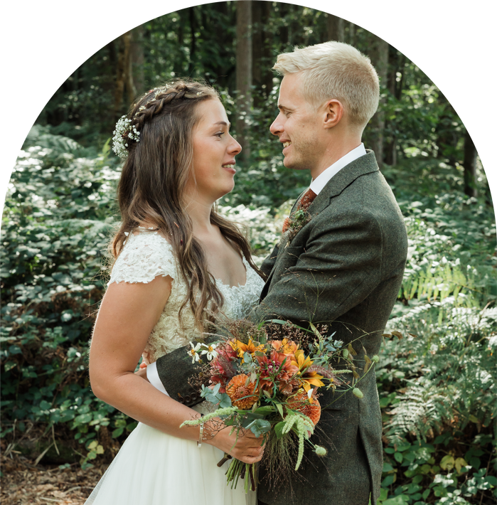 A bride and groom are looking into each other 's eyes while holding a bouquet of flowers.
