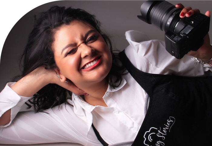 A woman in an apron is holding a camera and smiling