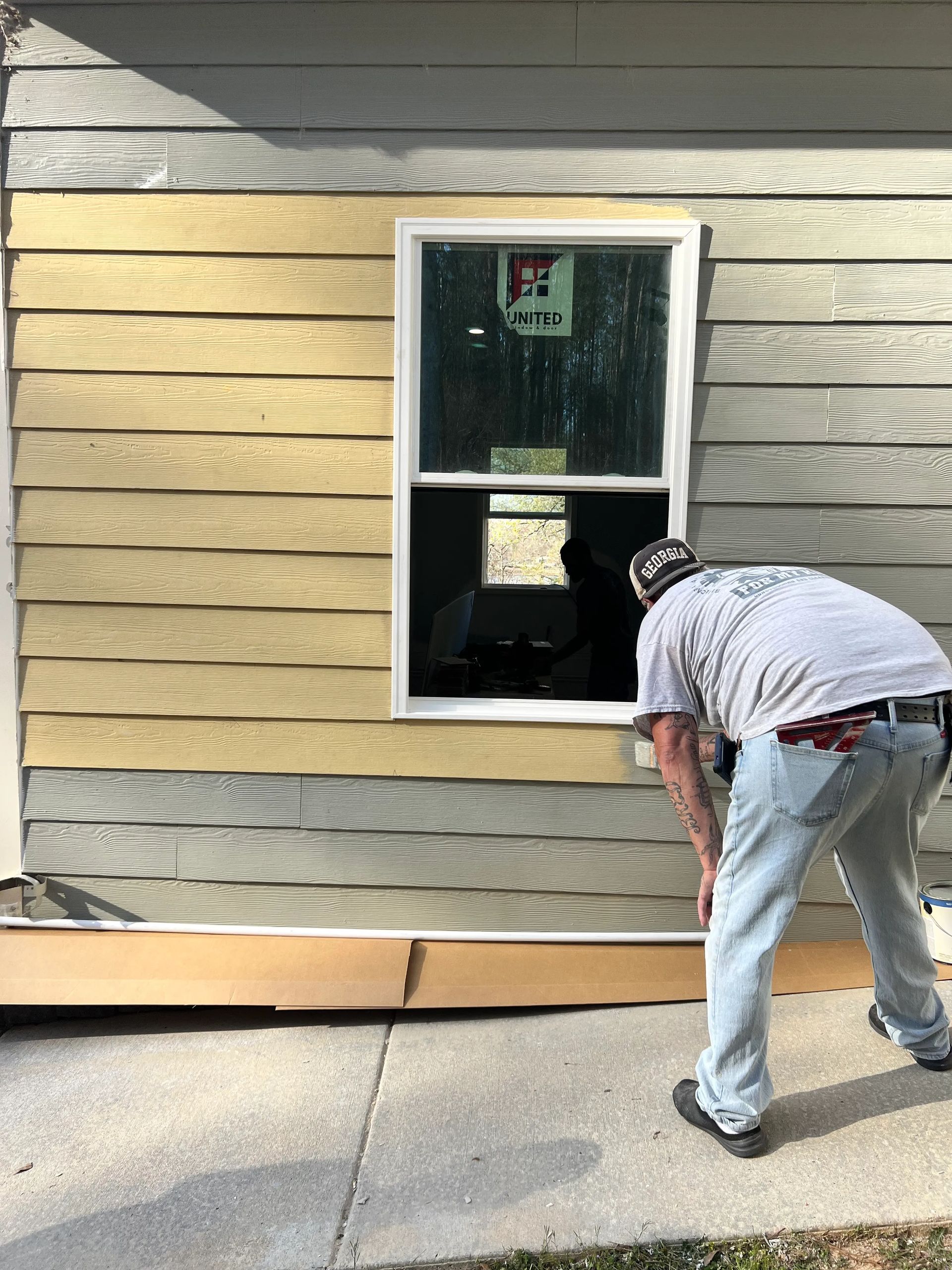A man is painting a window on the side of a house.