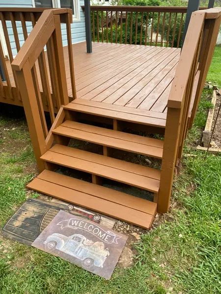 A wooden deck with stairs and a welcome mat on the ground.
