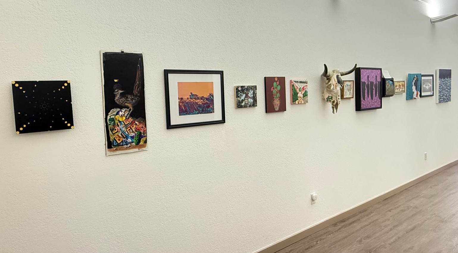A gallery wall featuring a variety of framed artworks, prints, and a decorative animal skull displayed on a white wall.