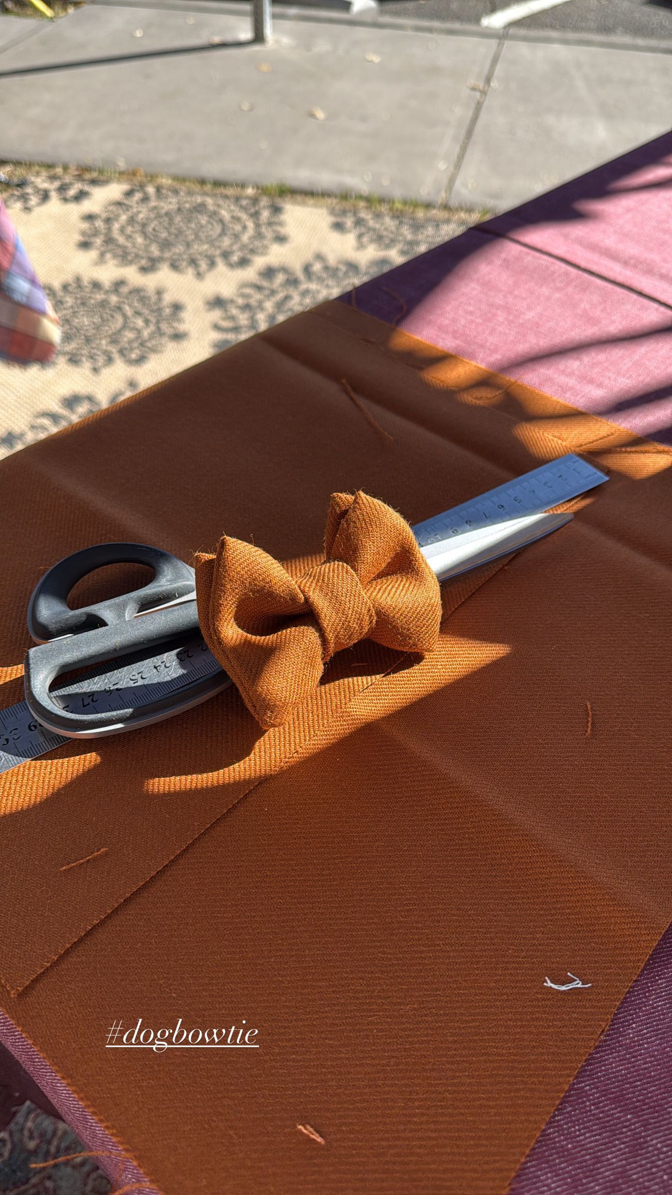 A textured, burnt-orange fabric bow sits on a matching piece of fabric, with a pair of metal scissors placed nearby.