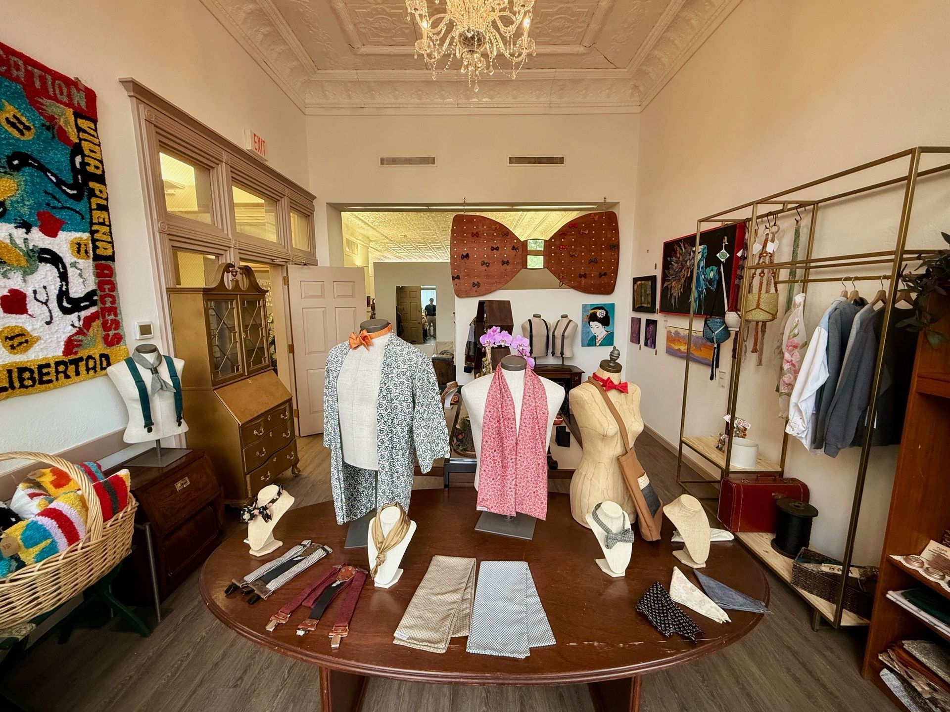 A boutique interior with clothing displayed on mannequins, a central wooden table, and hanging racks of garments.