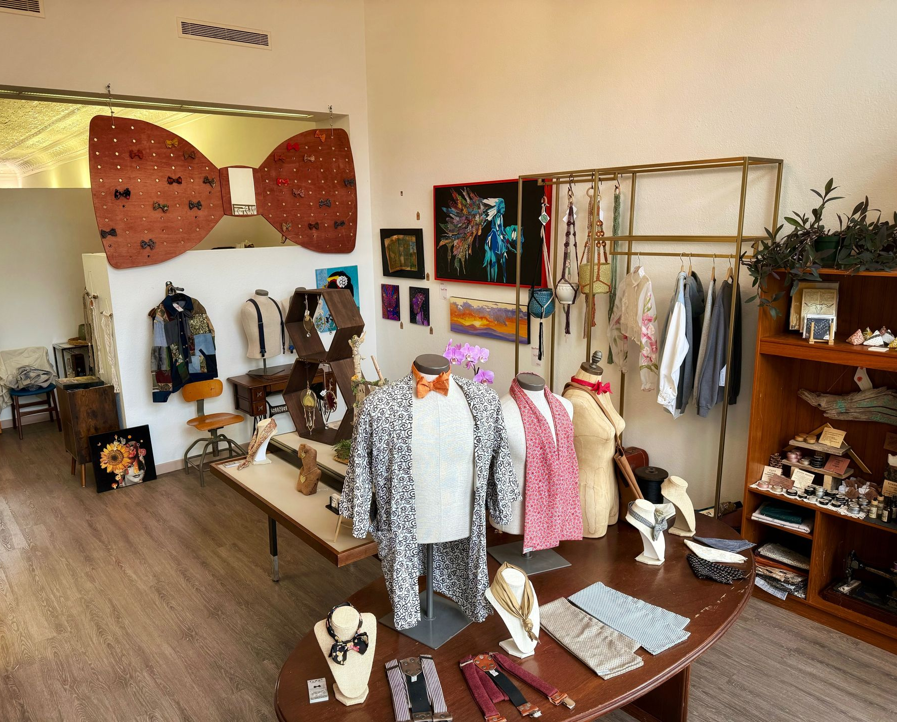 A boutique interior featuring clothing displays, mannequins, jewelry on tables, and a large bow-shaped wall art piece.