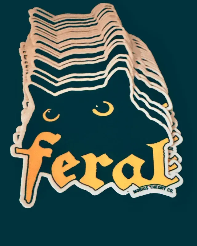 A stack of die-cut stickers featuring a black cat’s eyes and ears with the word 