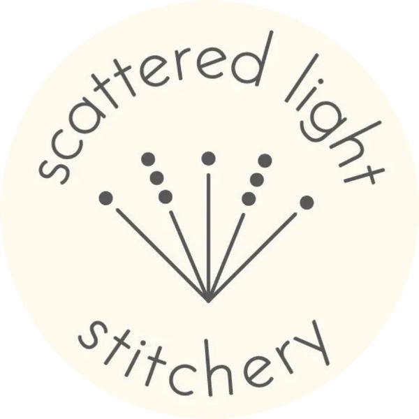 Logo for Scattered Light Stitchery with text arranged in a circle around an icon of five lines tipped with small dots.