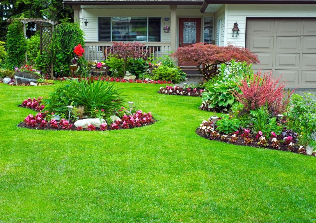 Beautifully landscaped front yard with manicured lawn, flower beds, shrubs, and a welcoming porch in front of a house.