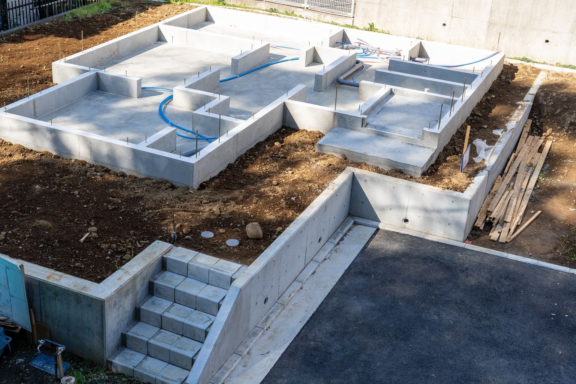 Concrete foundation of a building under construction, with steps leading down to a driveway.