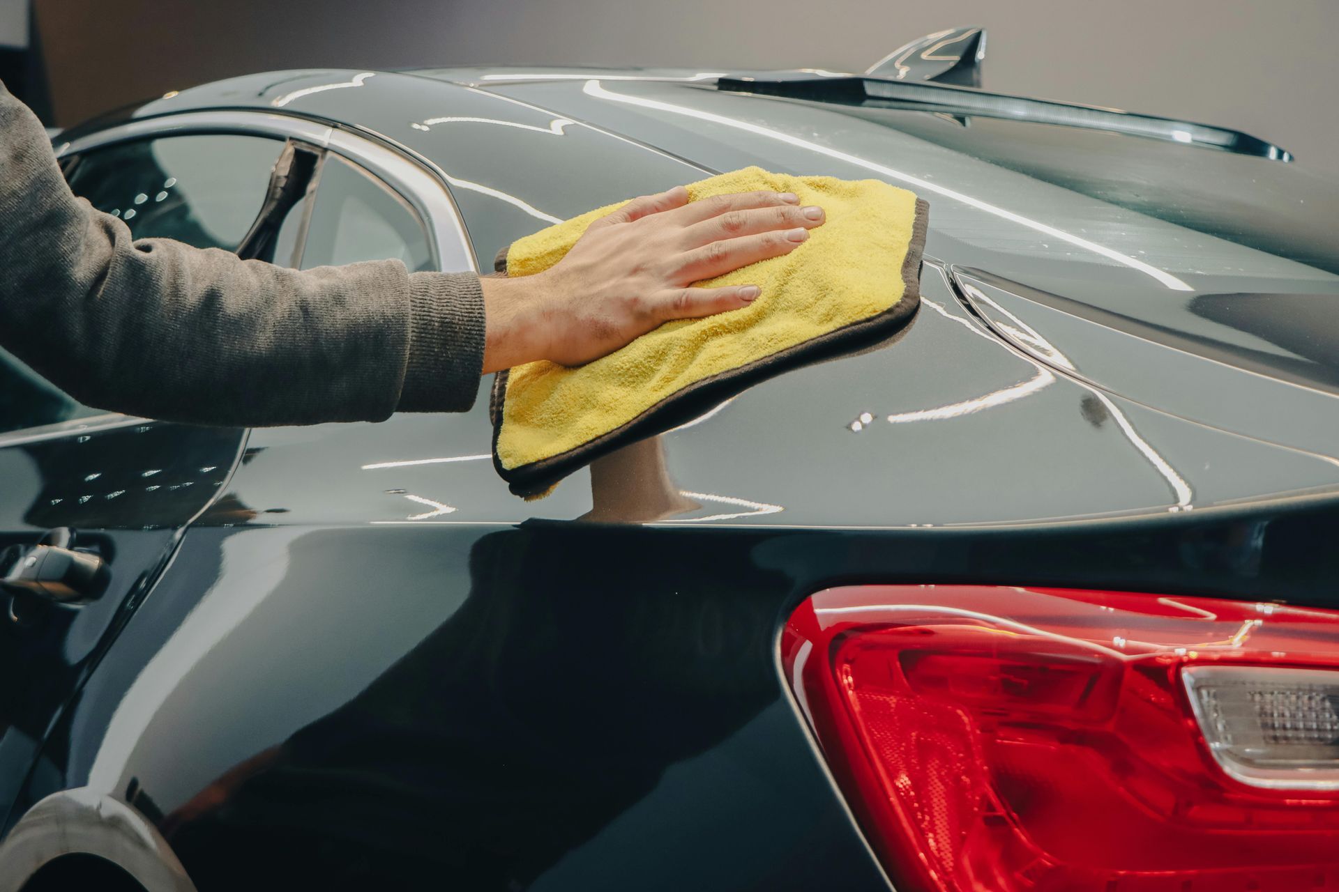Person wiping a black car's body with a yellow microfiber cloth.