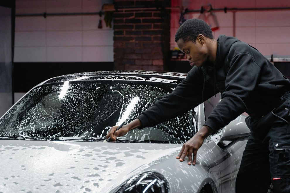 Man washing a white car with soapy water; smiling in a garage setting.