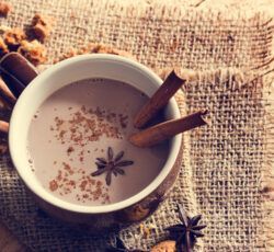 A cup of hot chocolate with cinnamon sticks and star anise on a table.