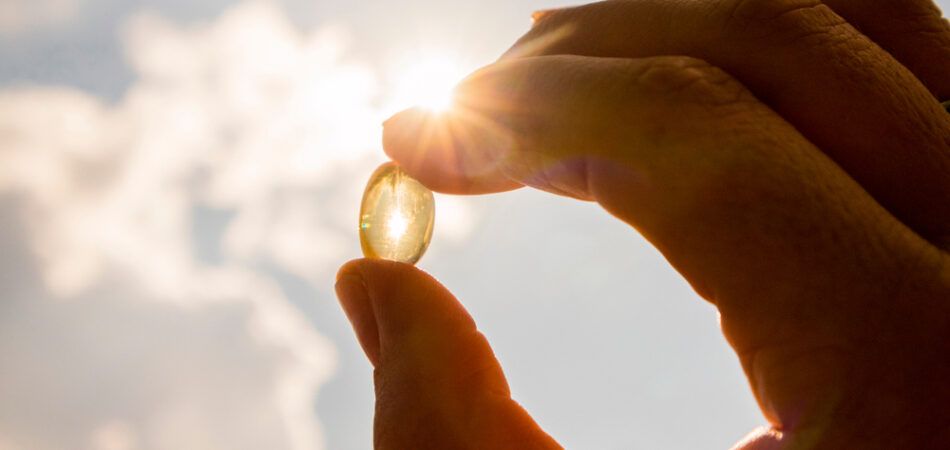 A person is holding a pill in their hand in front of the sun.