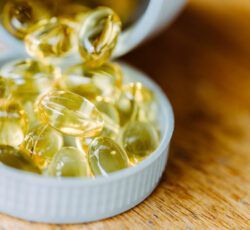 A bottle of fish oil capsules is being poured into a small bowl on a wooden table.