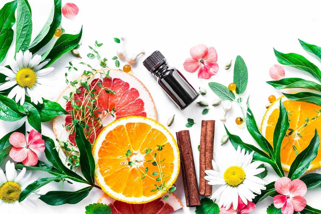 A bottle of essential oil surrounded by fruits and flowers on a white background.