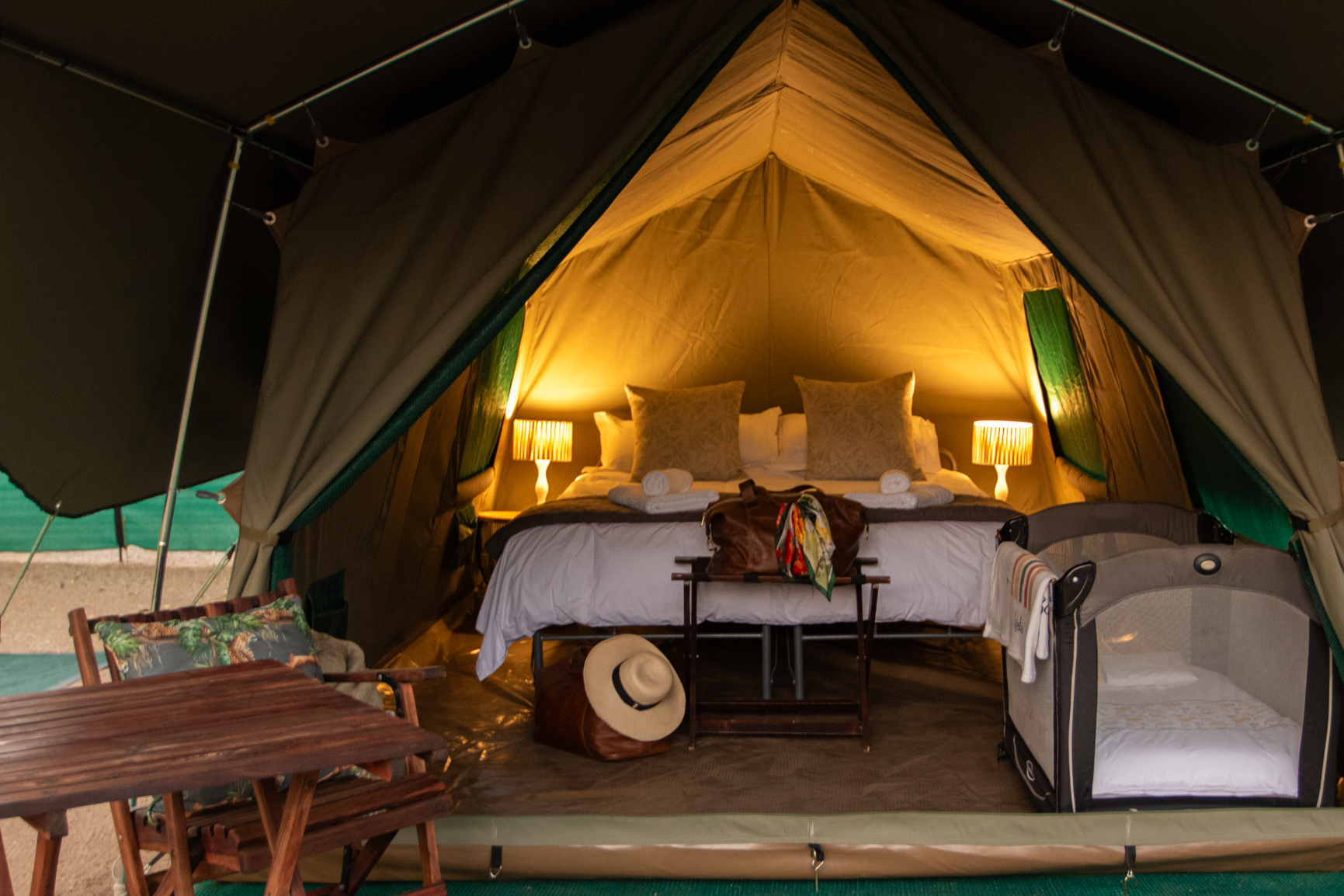 A clamping tent in the Kruger National Park with a bed , table , chairs and a crib inside of it.