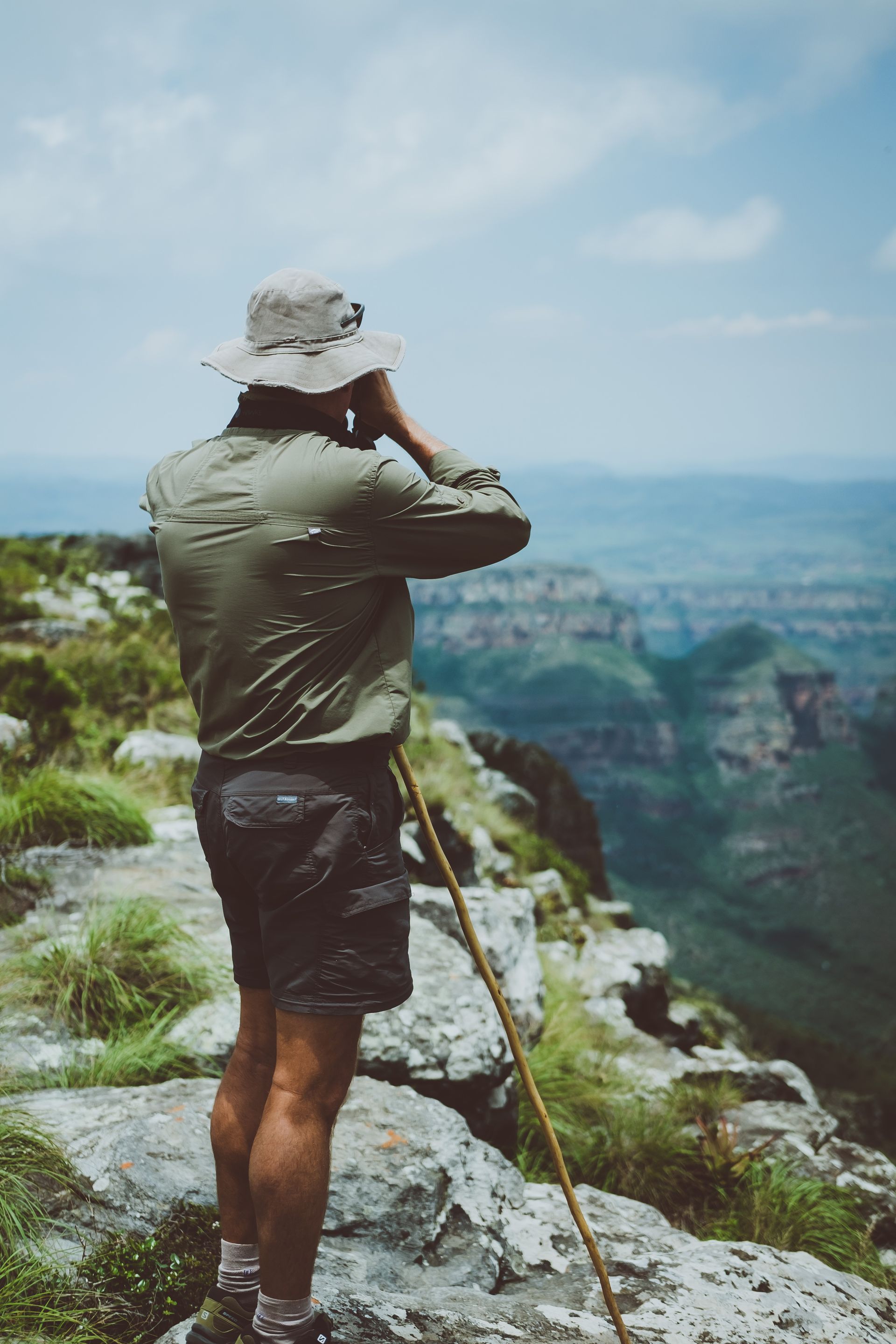 A man is standing on top of a mountain looking through binoculars.