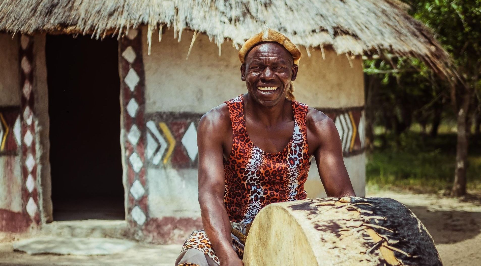a man is sitting on a drum in front of a thatched hut .