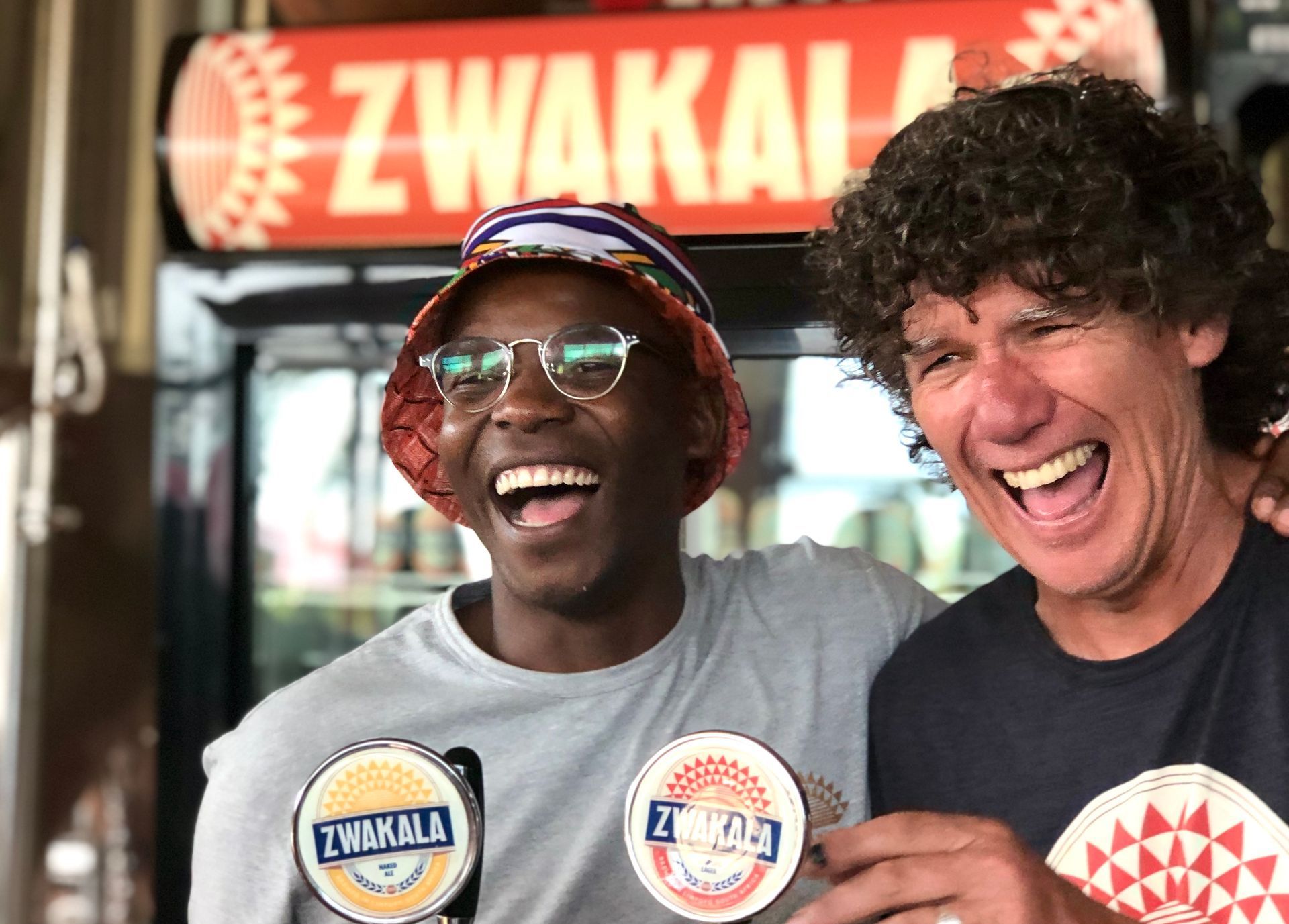 two men are posing for a picture in front of a zwakala fridge .