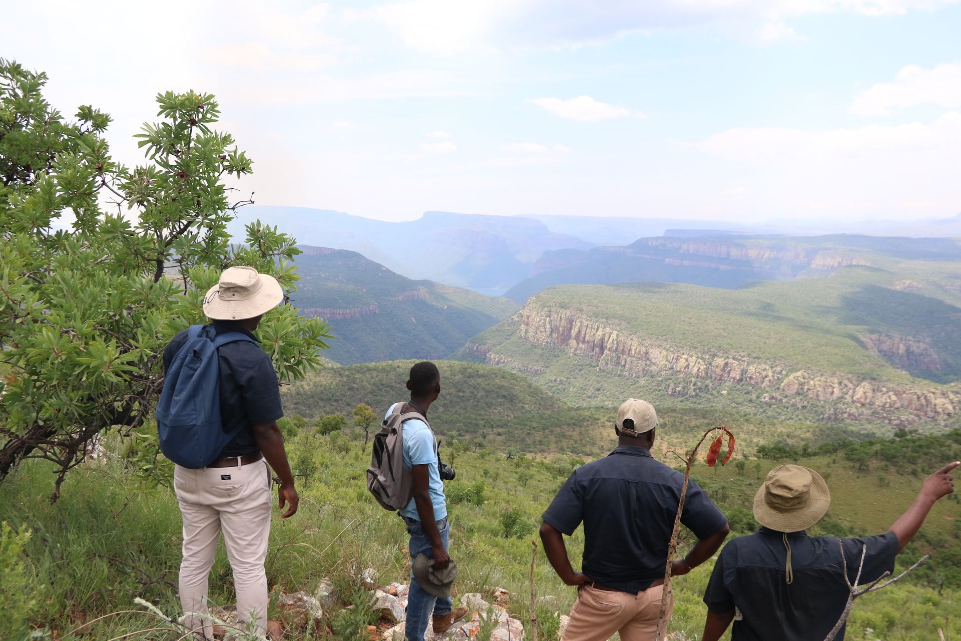 Three men are standing on top of a hill looking at the mountains.