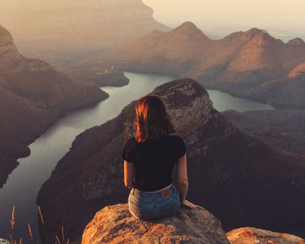 A woman is sitting on top of a mountain overlooking a river.